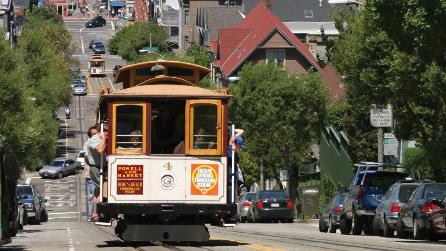 A trolly moving along a city street with water and island, and boats, in the distance.