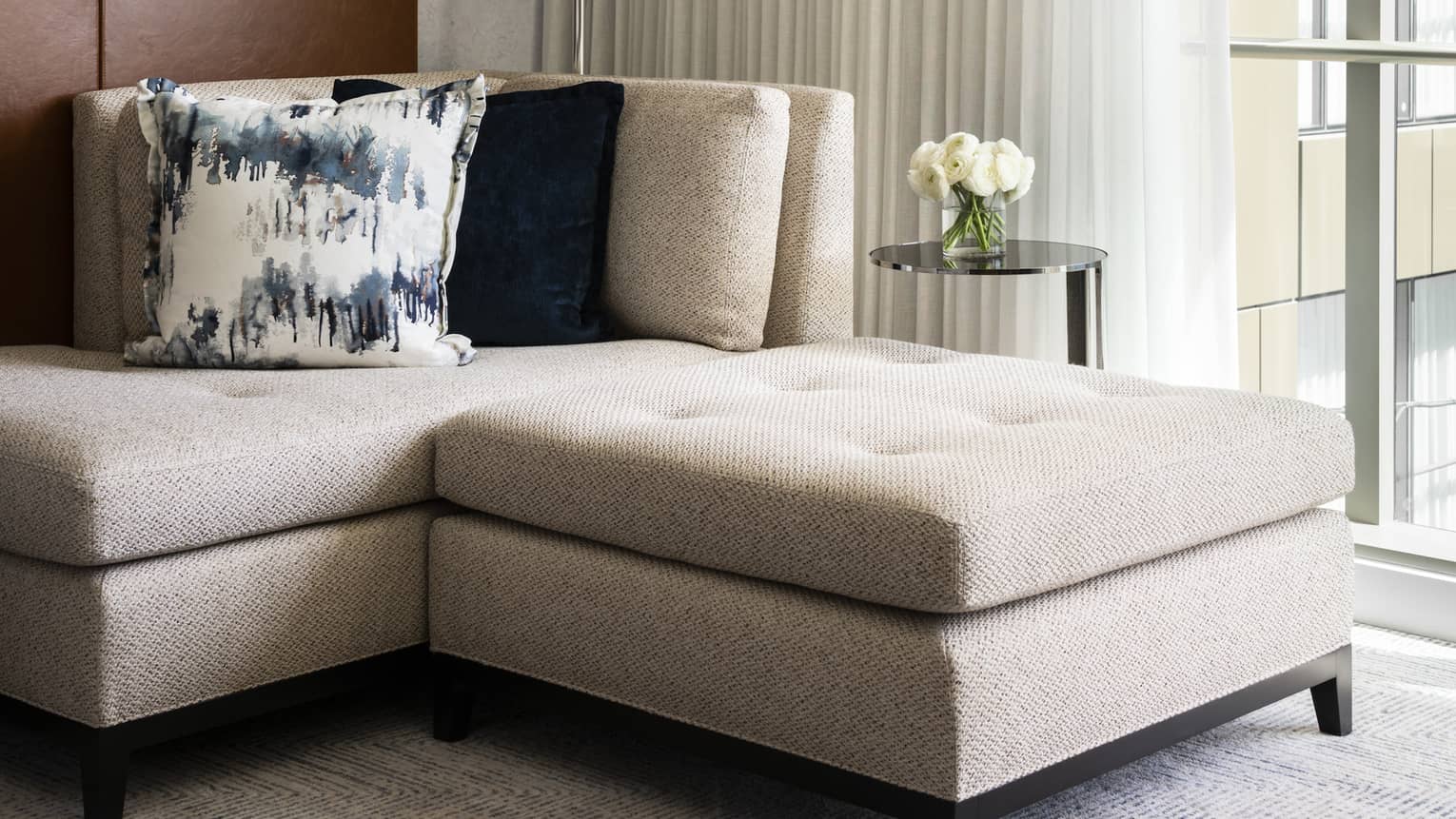 White flowers sit on a table next to a couch with plush cushions
