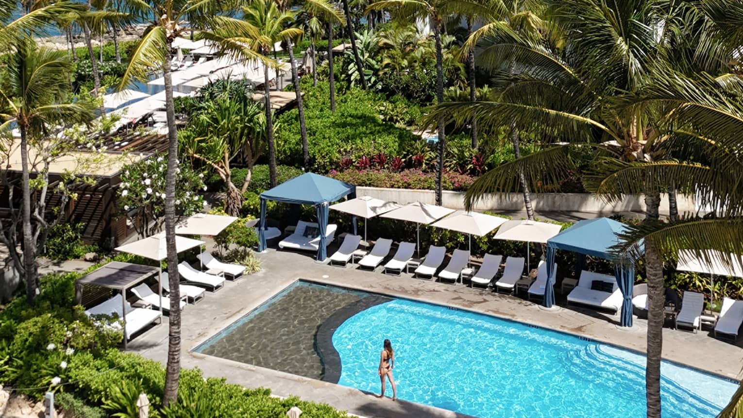 Family pool at luxury Hawaiian resort, lined with beach chairs and cabanas