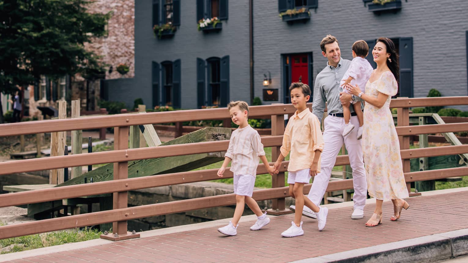 Man, woman, and three young children walk along a sidewalk over a bridge