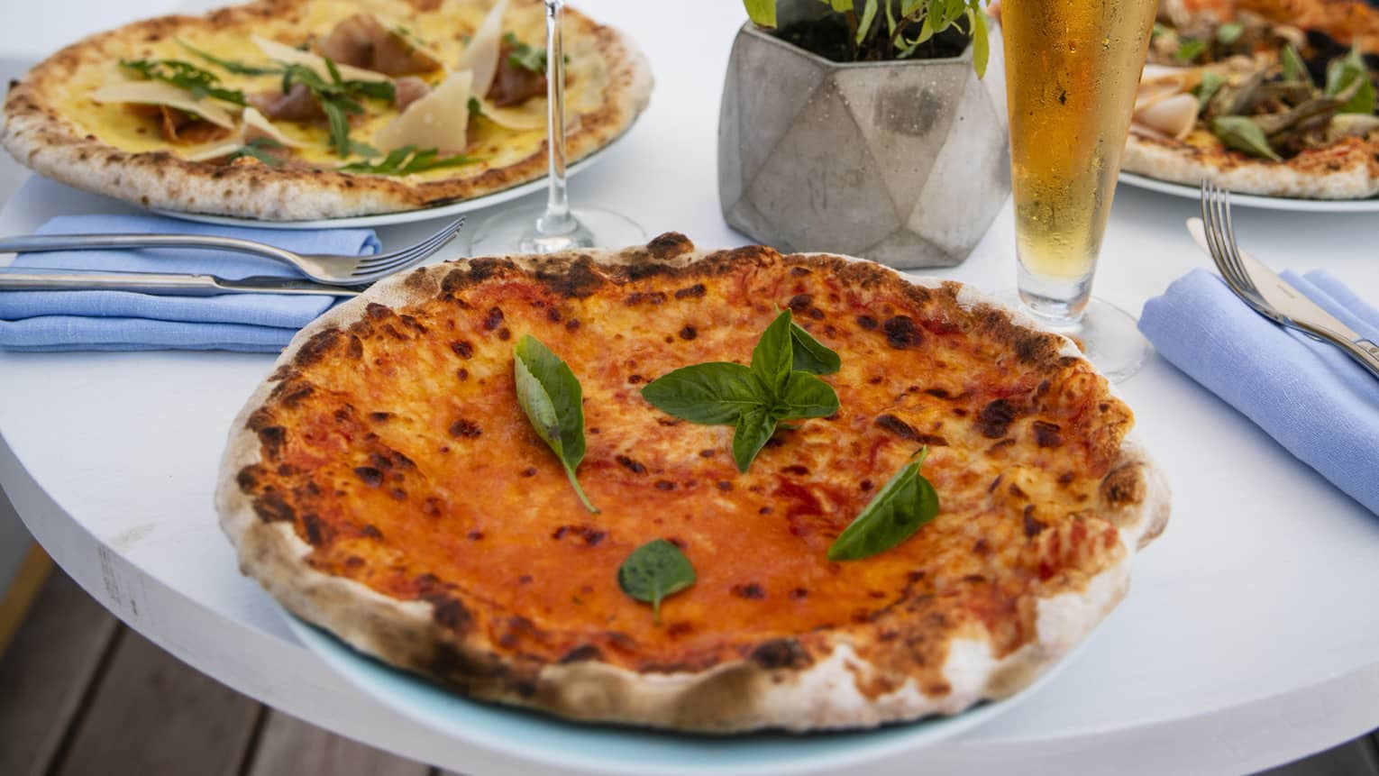 A table set with a glass of rose and a pilsner of beer with craft pizzas on it overlooking the beach at Four Seasons Maldives - Landa