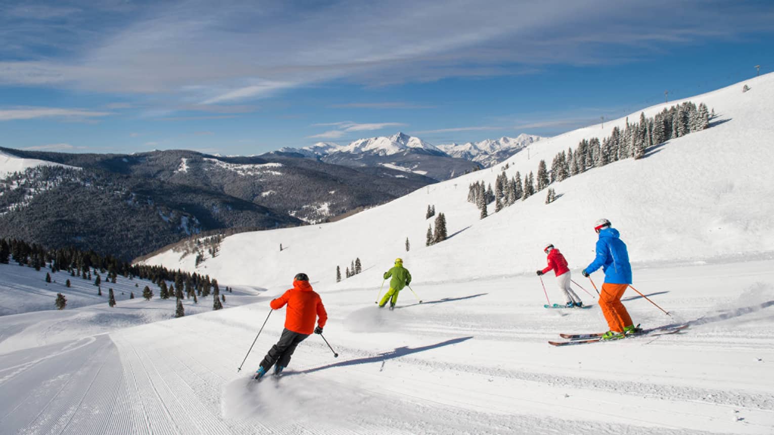 Four skiers in brightly coloured coats ski down mountain covered in snow