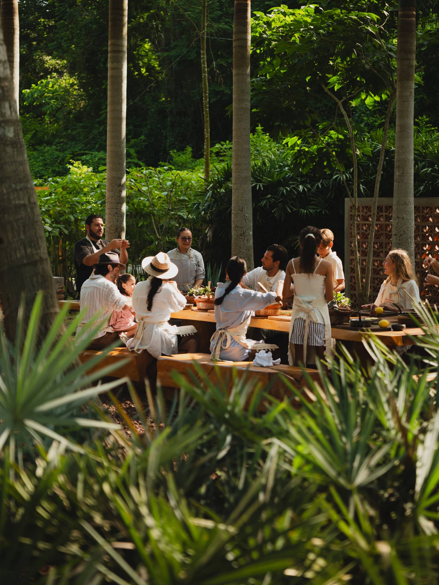 People seated around a long outdoor dining table set among palm trees