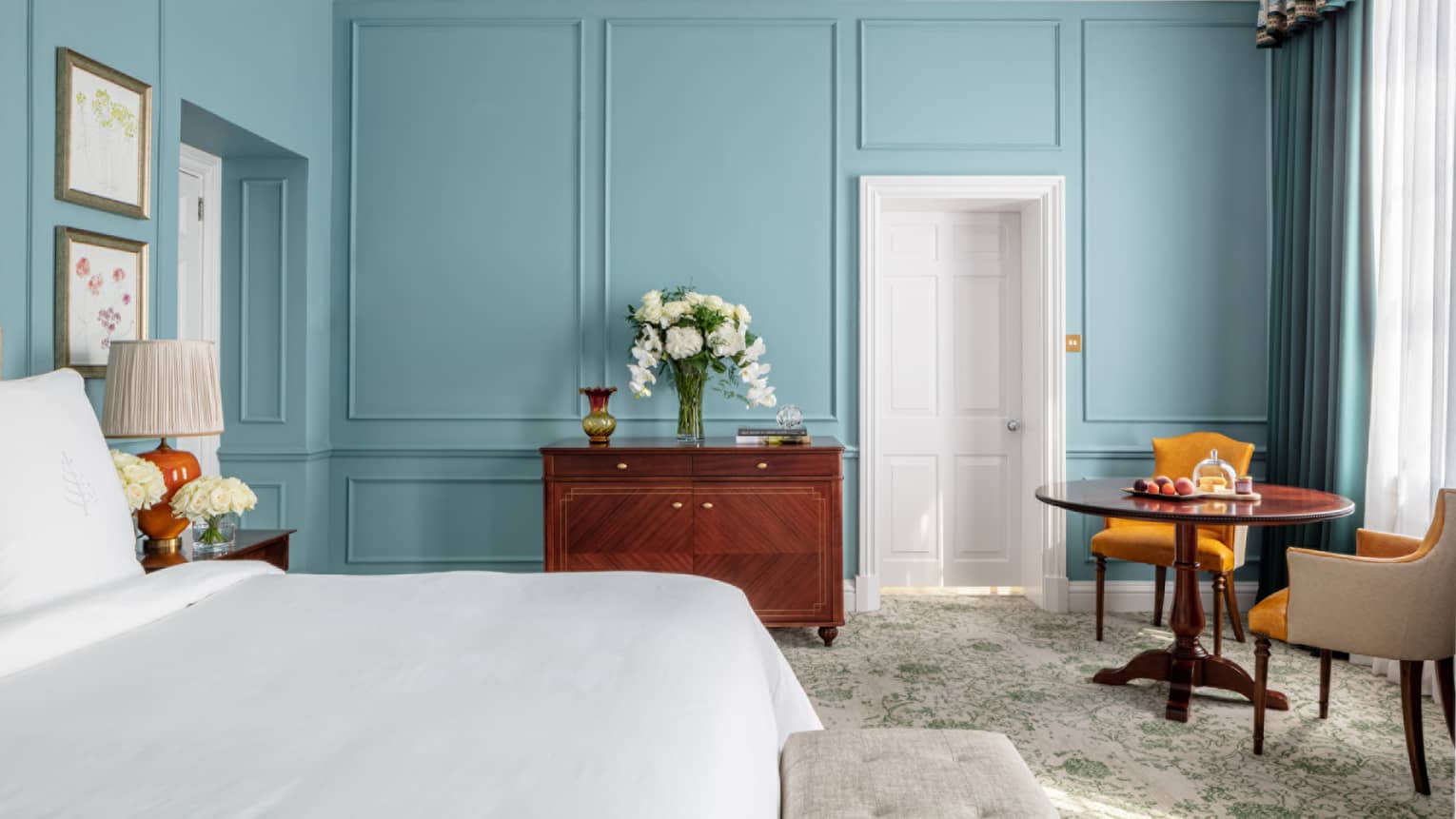 Guest room with Queen bed, white linens, paisley carpeting, cherry wardrobe, accent table for two, turquoise walls