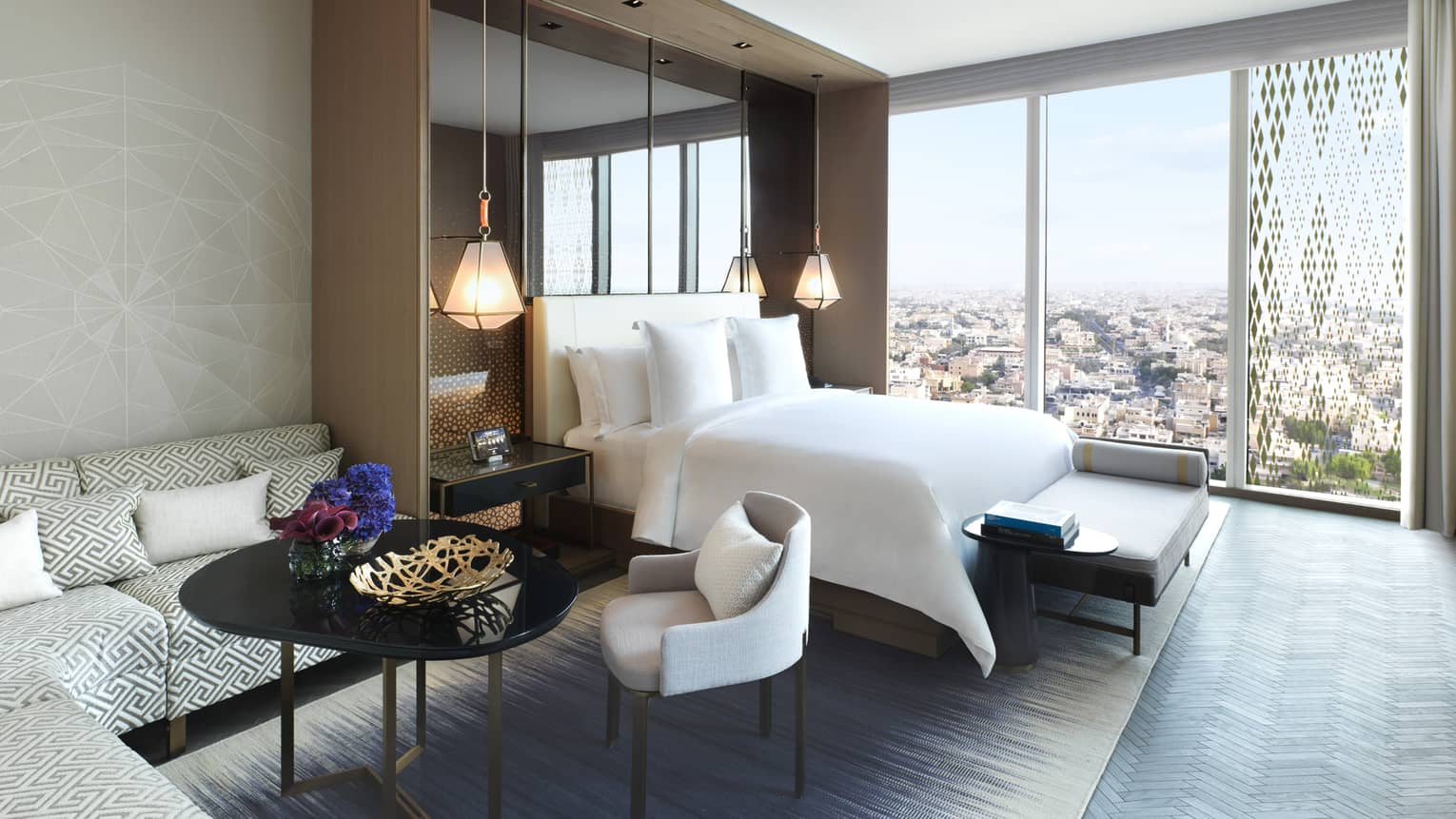 Ambassador Suite L-shaped sofa, table and chair beside bed, floor-to-ceiling window