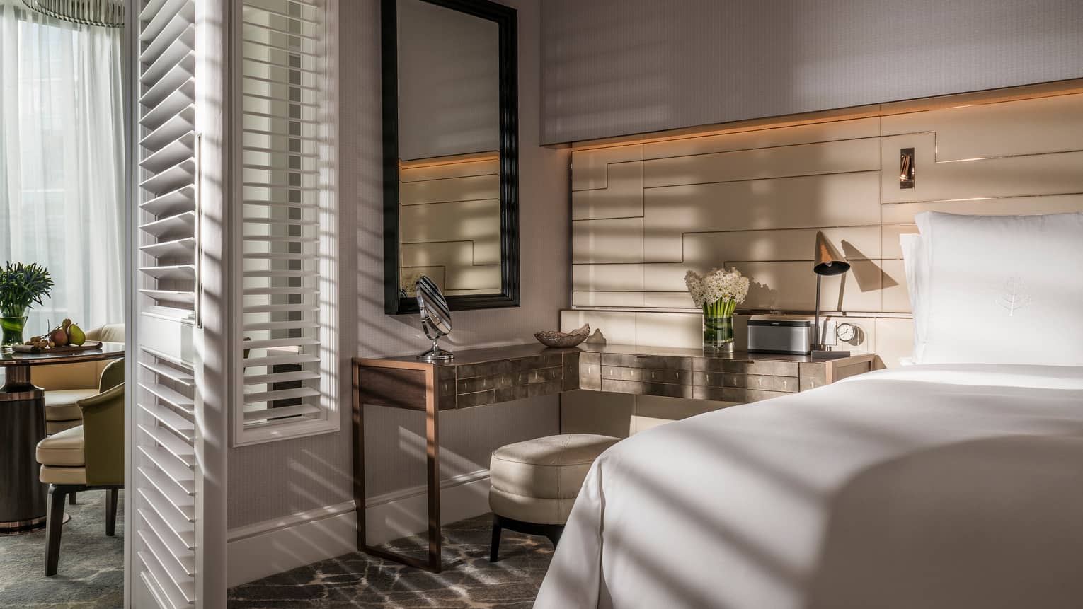 Sun streams into bedroom through tall white California shutters on dining room wall