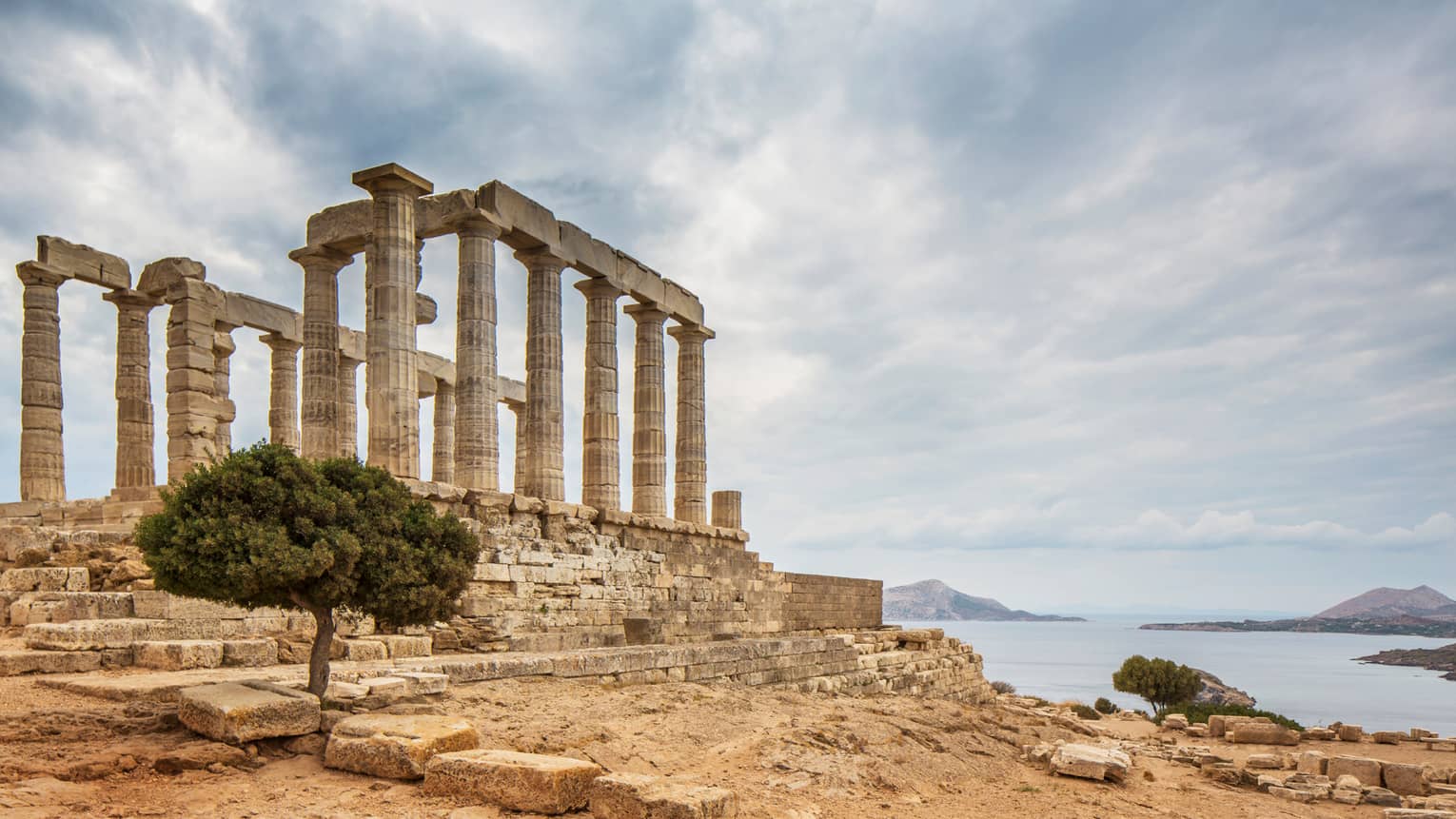 Ancient ruins stand near water under sky with clouds