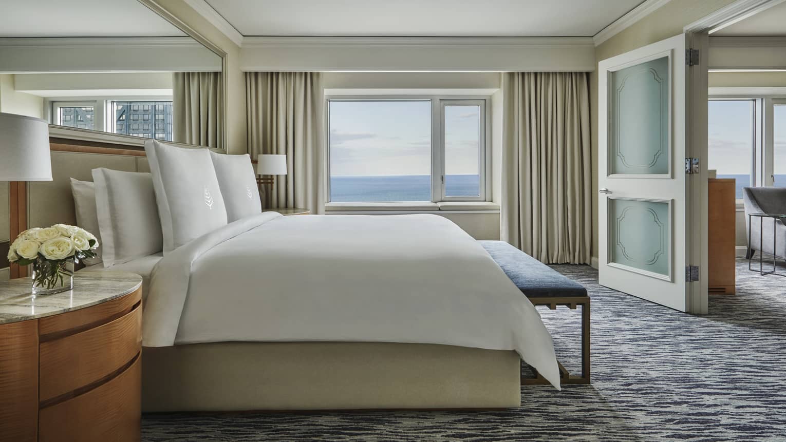 Bedroom with king bed room, large mirror over bed, wooden side table, sea view, opens to living room