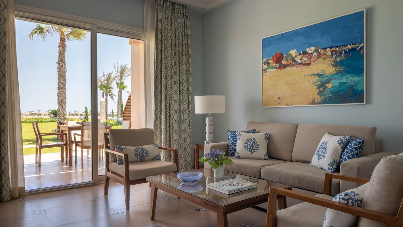 Living area with tan sofa, rectangular coffee table, twin arm chairs, sliding glass table to patio with dining set