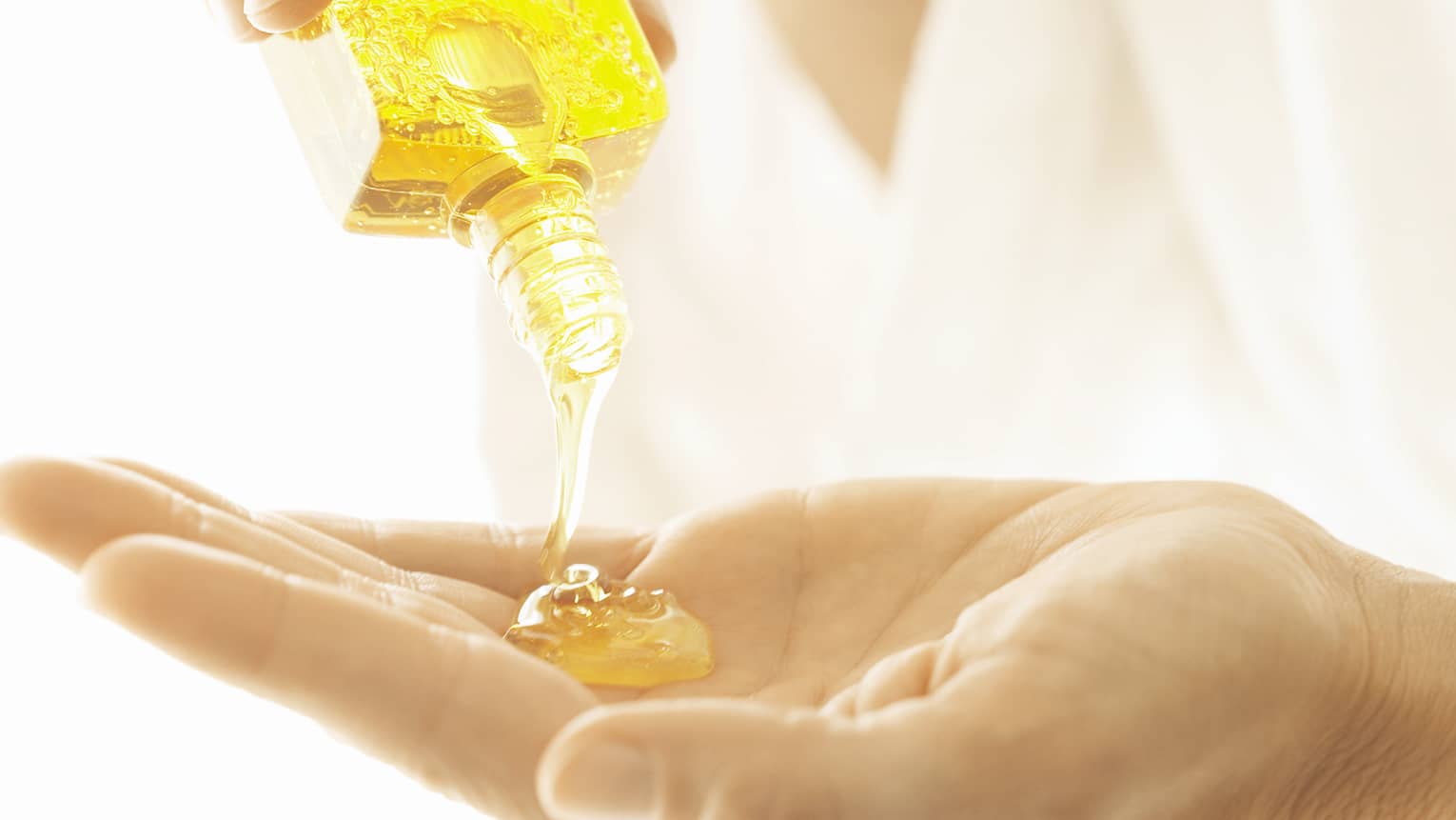 A close up of a woman's hands, pouring oil into her hand.