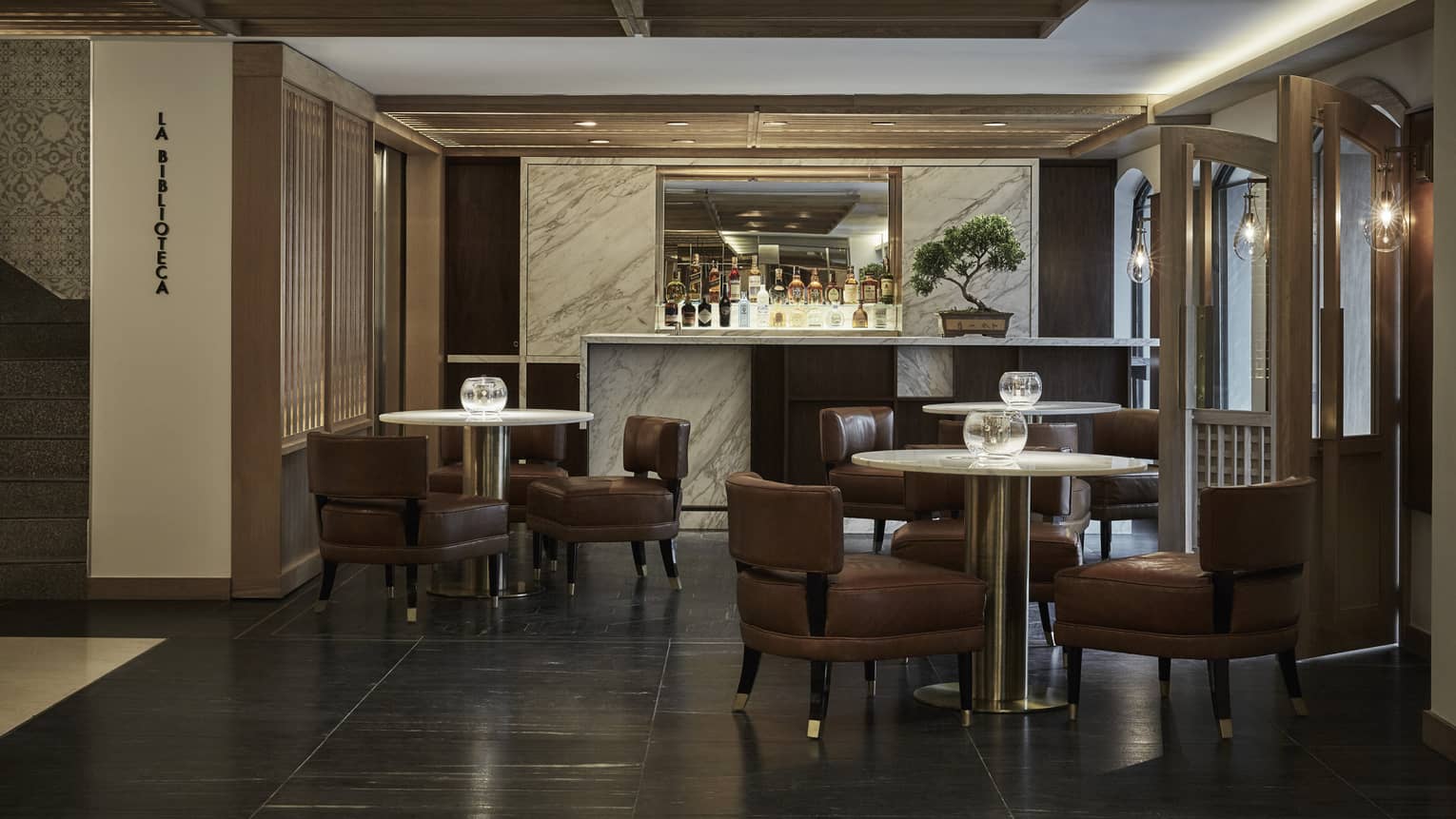 A dimly lit lounge with burgundy chairs and a fully stocked bar.