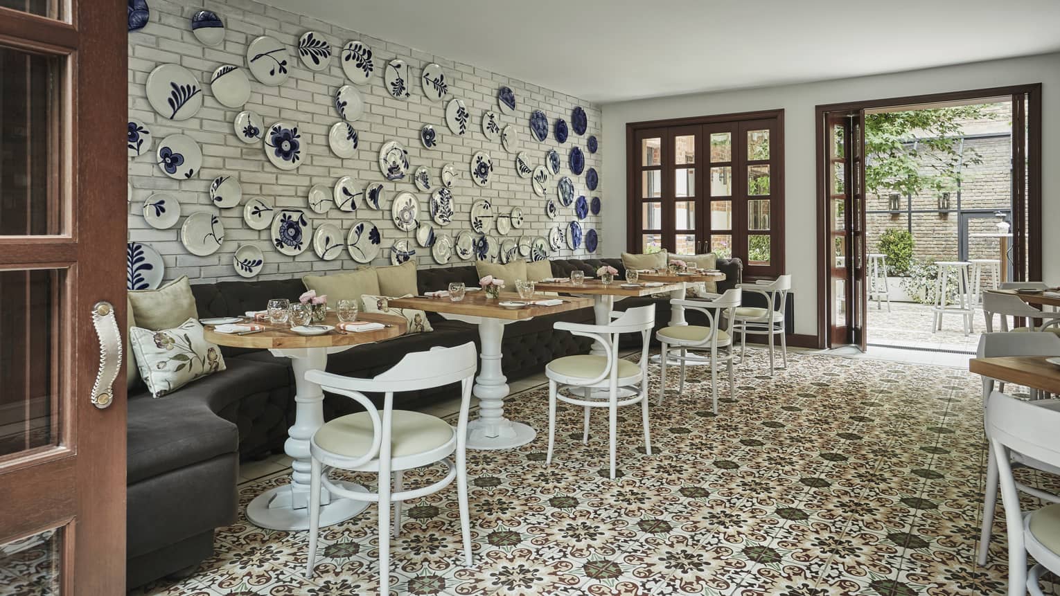 Blue-and-white decorative plates on wall over velvet banquette, cafe tables and chairs, tile floor