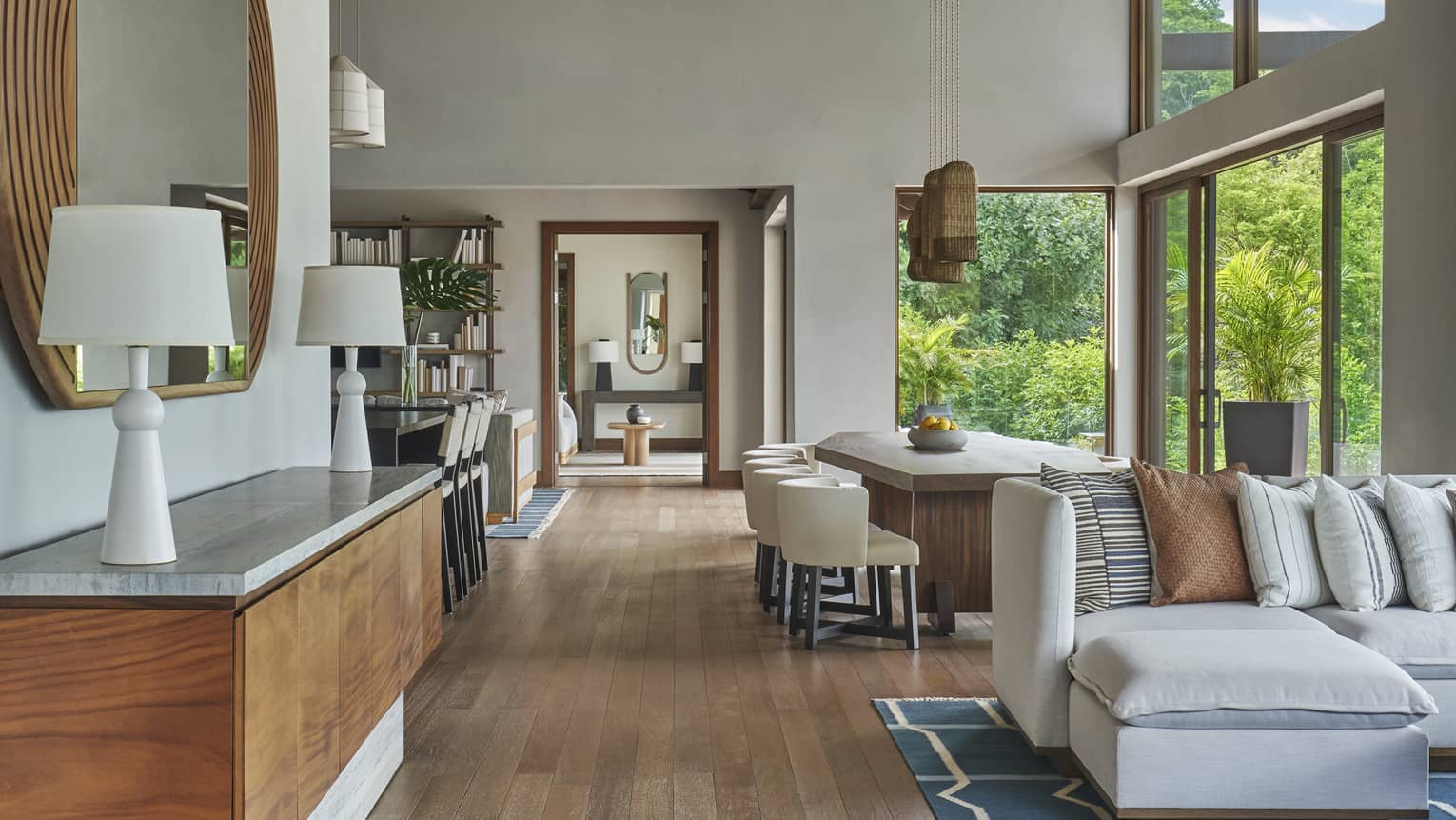 Living area with wooden floors, a light grey sofa, sideboard with two lamps, dining room