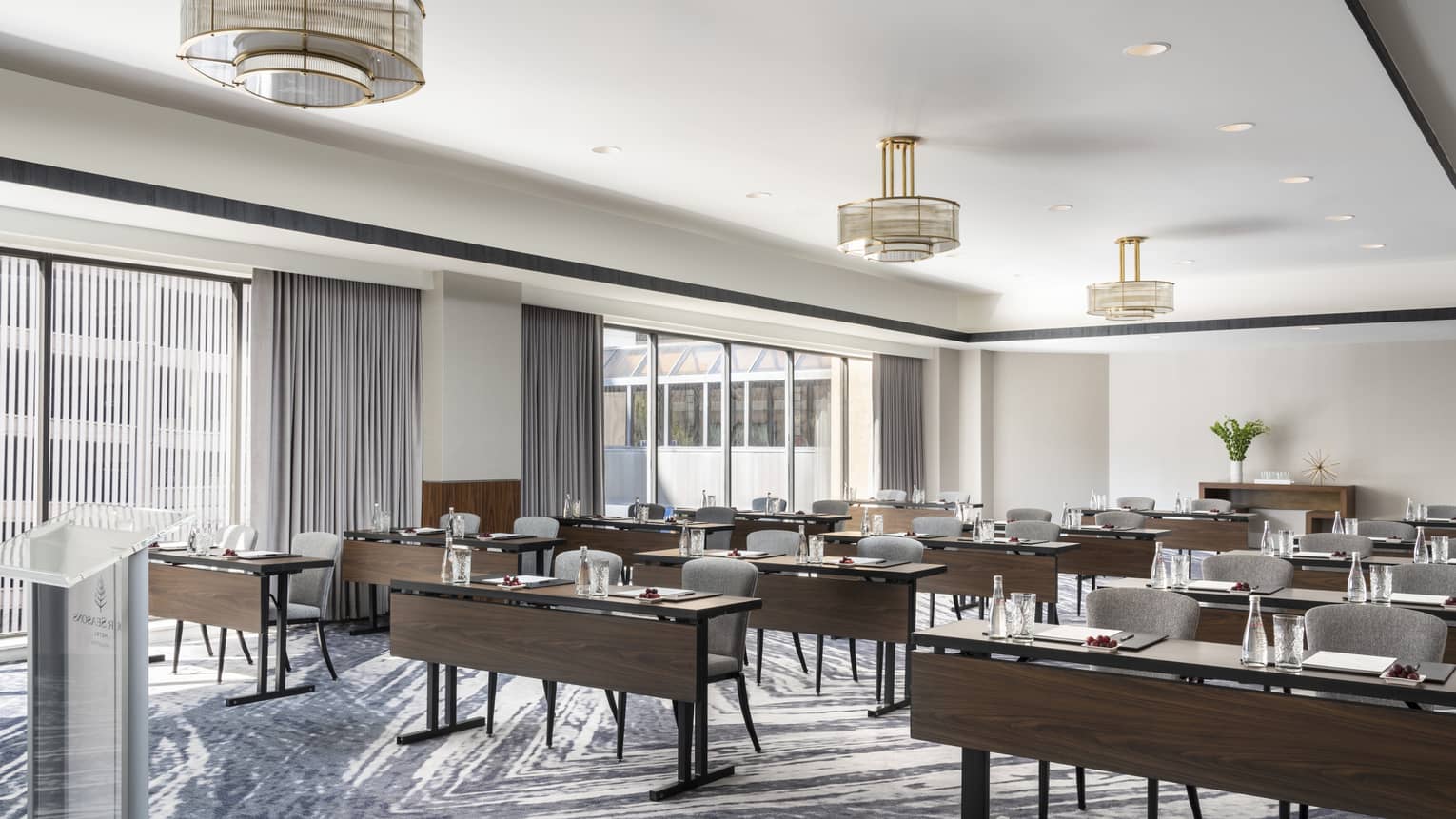 A well lit meeting room with dark wood tables and chairs facing a podium.