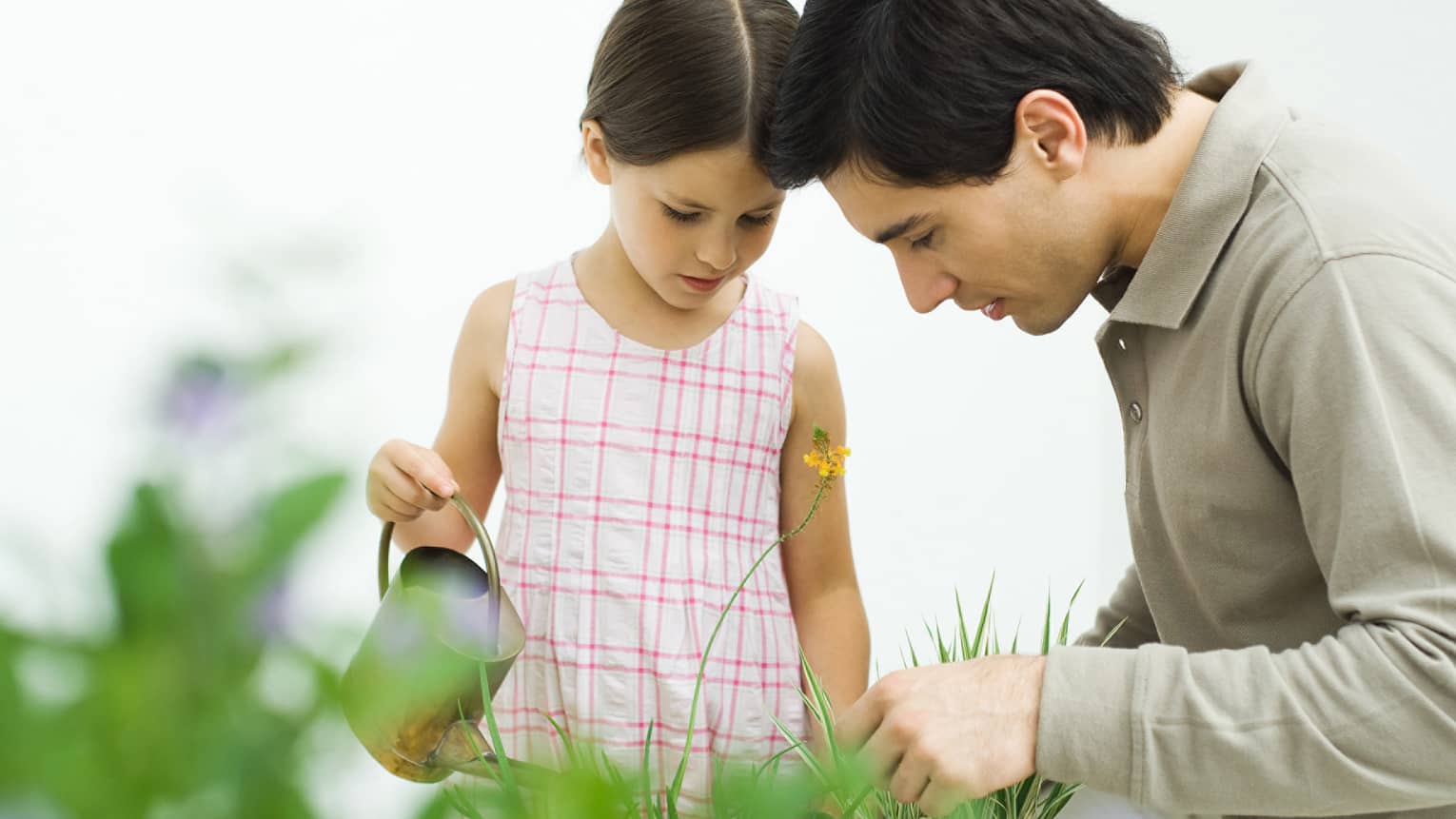 Man and young girl with watering can in tall grass, garden