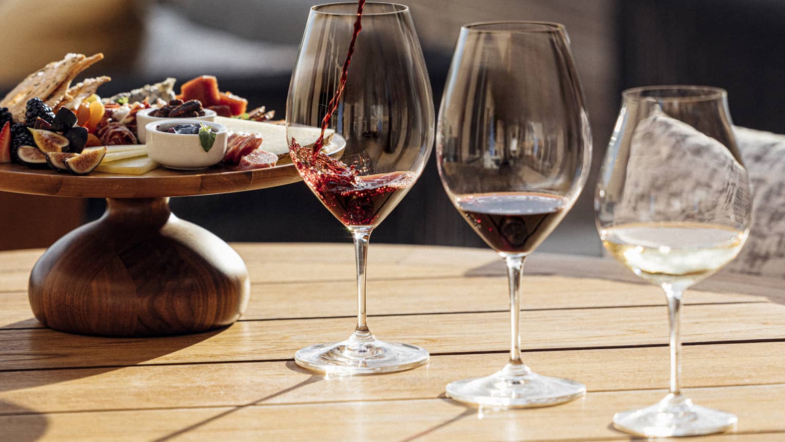 Three glasses of wine are poured next to a plate of charcuterie