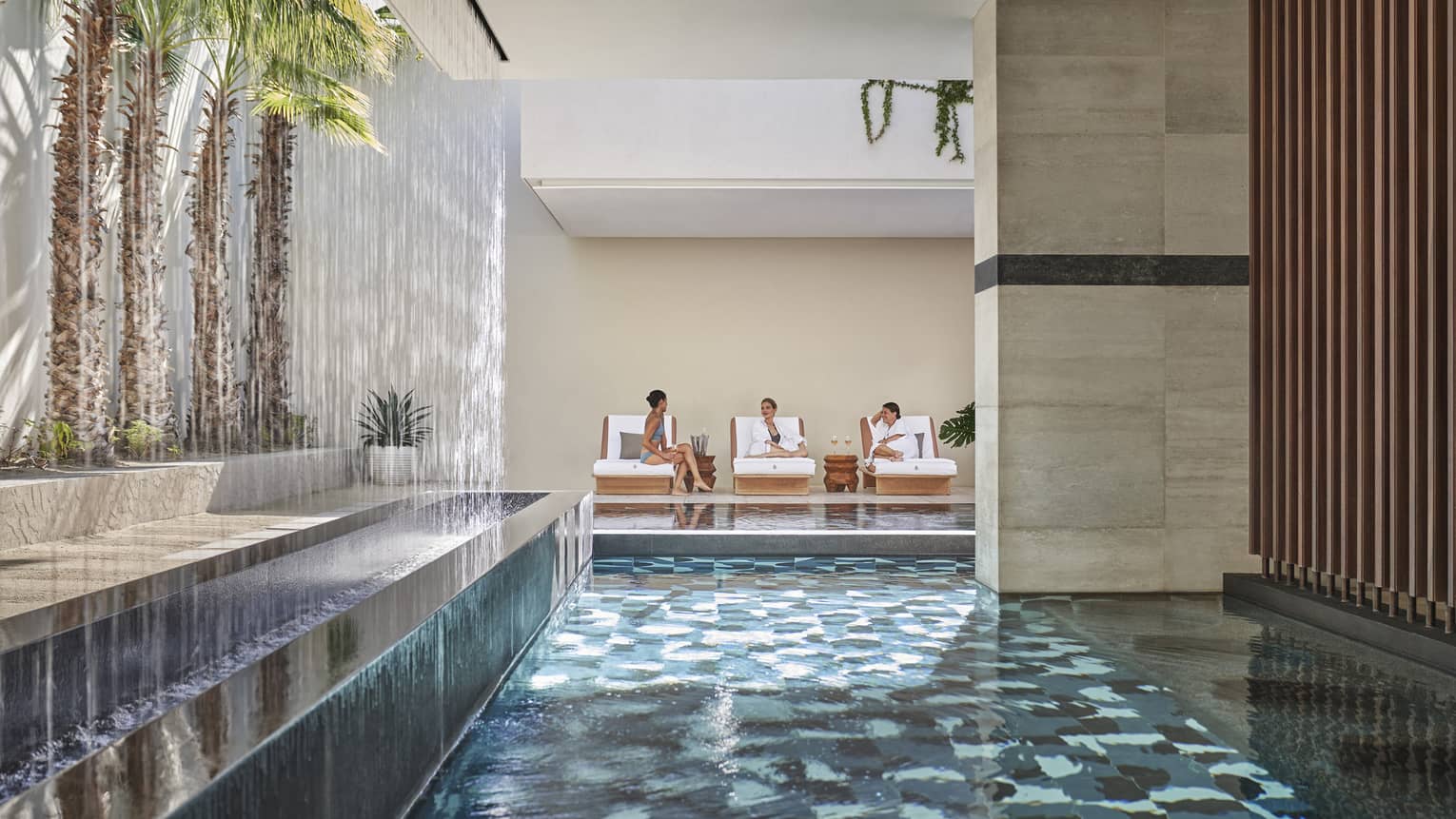 Three women in a spa by an indoor pool.