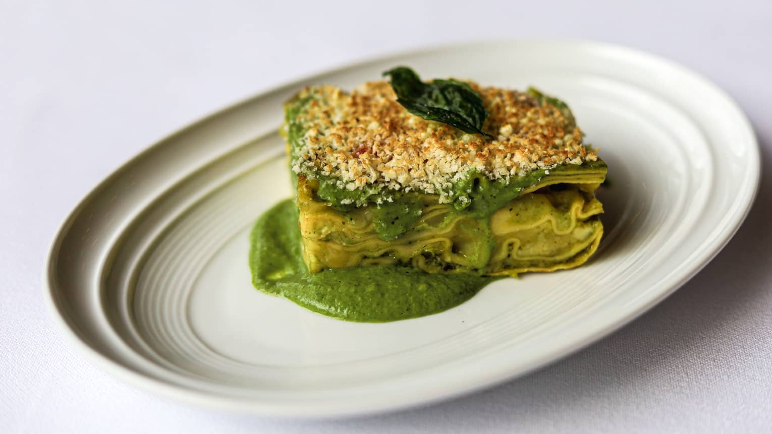 Fresh lasagna sheets layered with creamy pesto sauce gratinated with Parmigiano Reggiano on a white plate