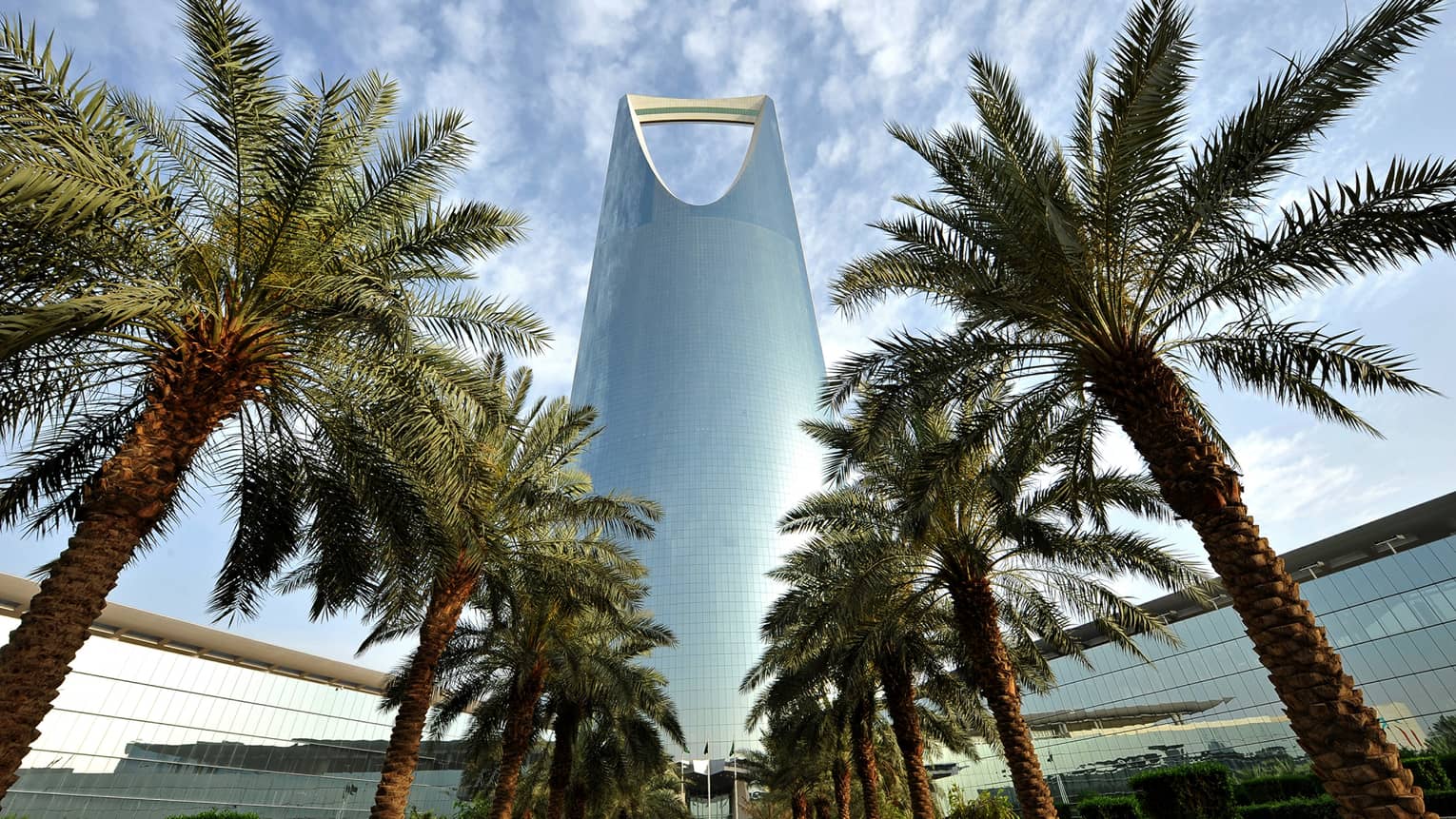 Looking up at modern Four Seasons Hotel Riyadh at Kingdom Centre tower skyscraper between rows of palm trees 