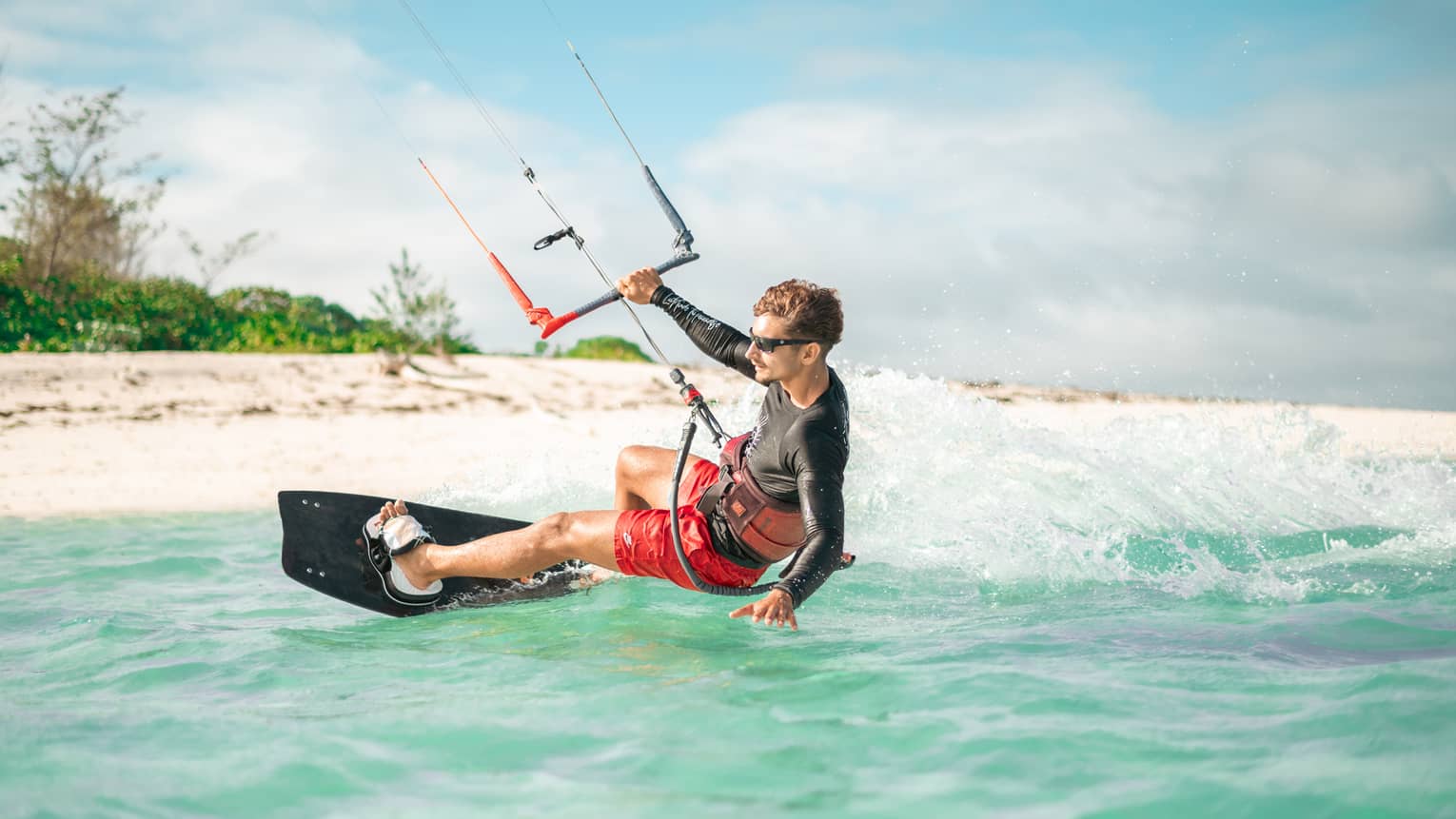 Person kite surfing atop blue-green waters by a white-sand beach