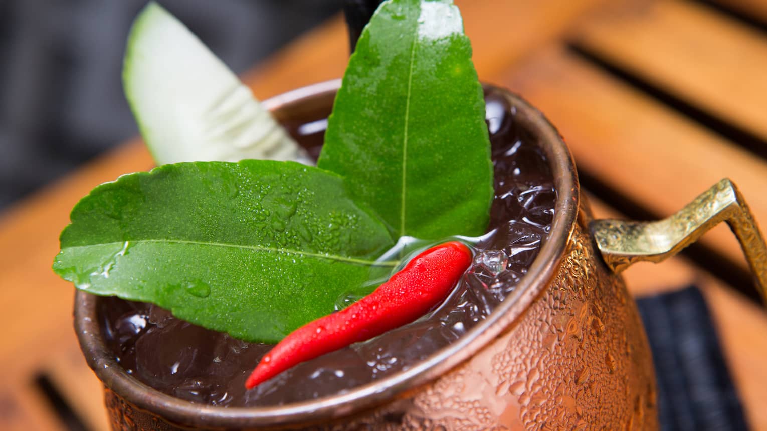 Close-up of green lime leaves, small red hot pepper on cocktail in brass cup