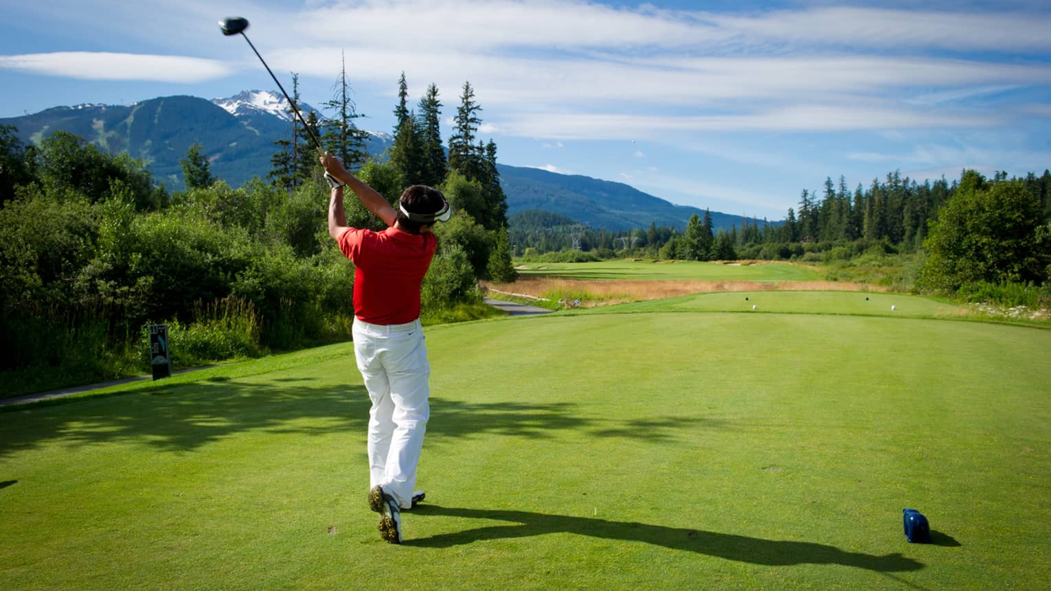 Back view of man swinging golf club on green, mountains in distance