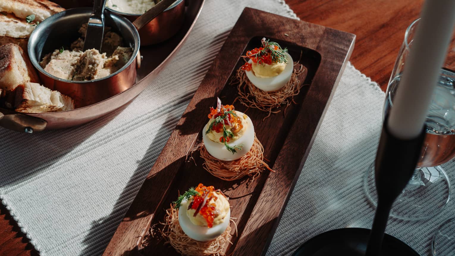 Three deviled eggs set on a dining table beside a glass of water and candle