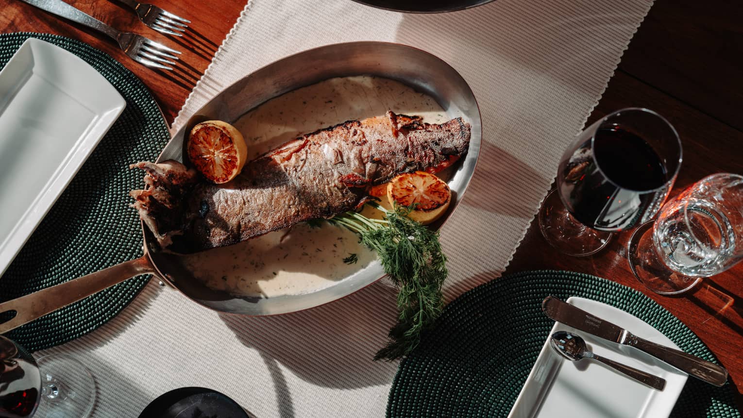  Arctic char set on a table beside wine glasses and silverware