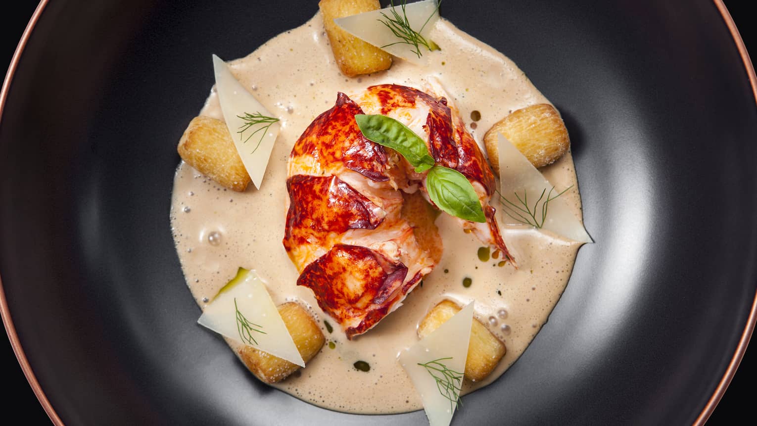 Lobster Two Ways entree, artistic presentation with lobster tail in sauce in dish, herb garnishes