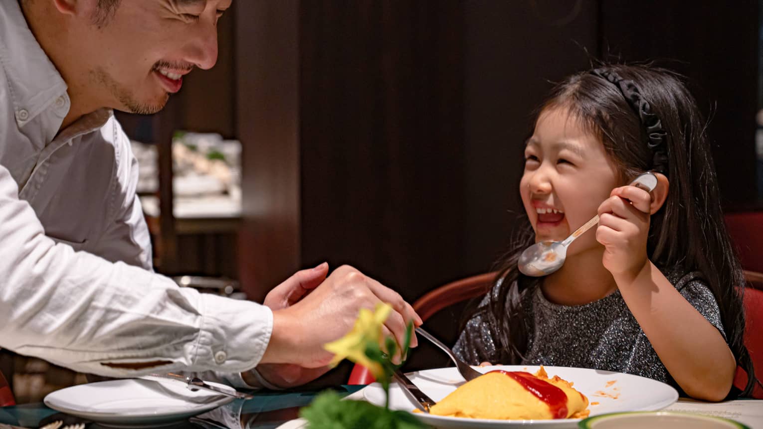 Smiling young girl and her dad dig into omurice topped with ketchup