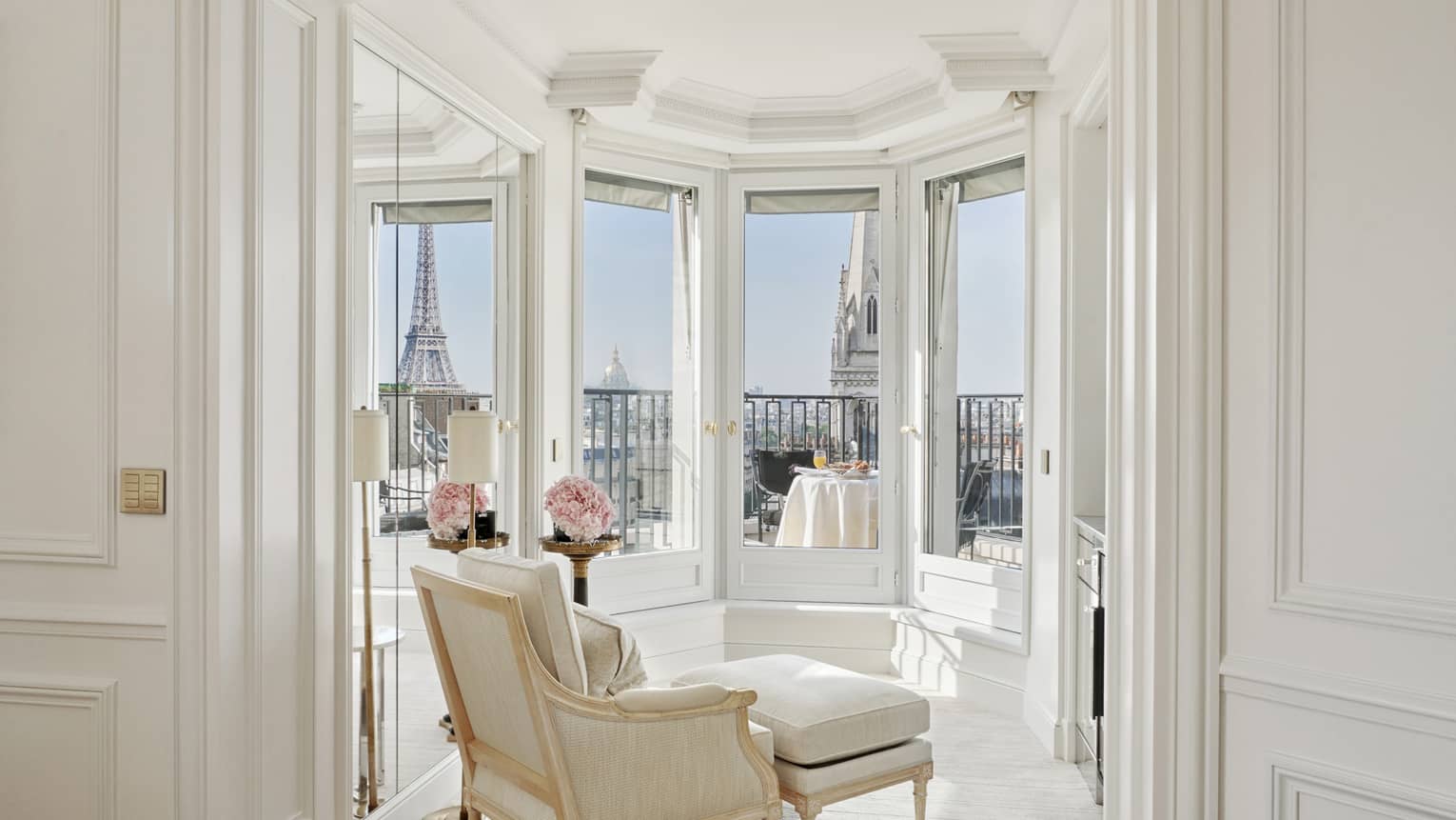 A white room has windows and a balcony with a direct view of the Eiffel Tower