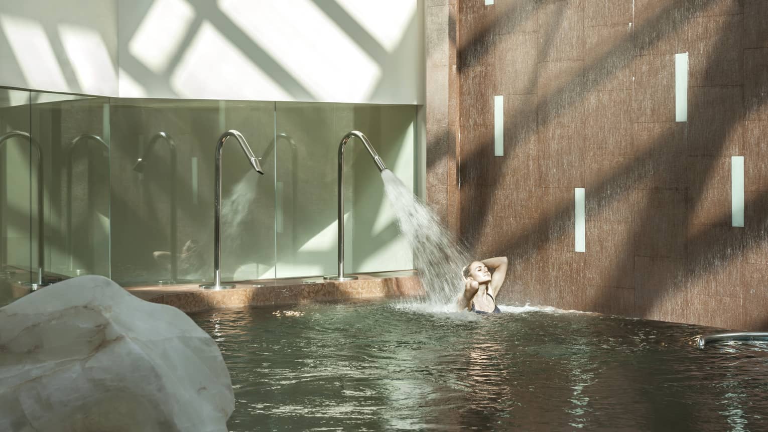 Woman wades in vitality pool as water sprays over her hair in Luceo Spa