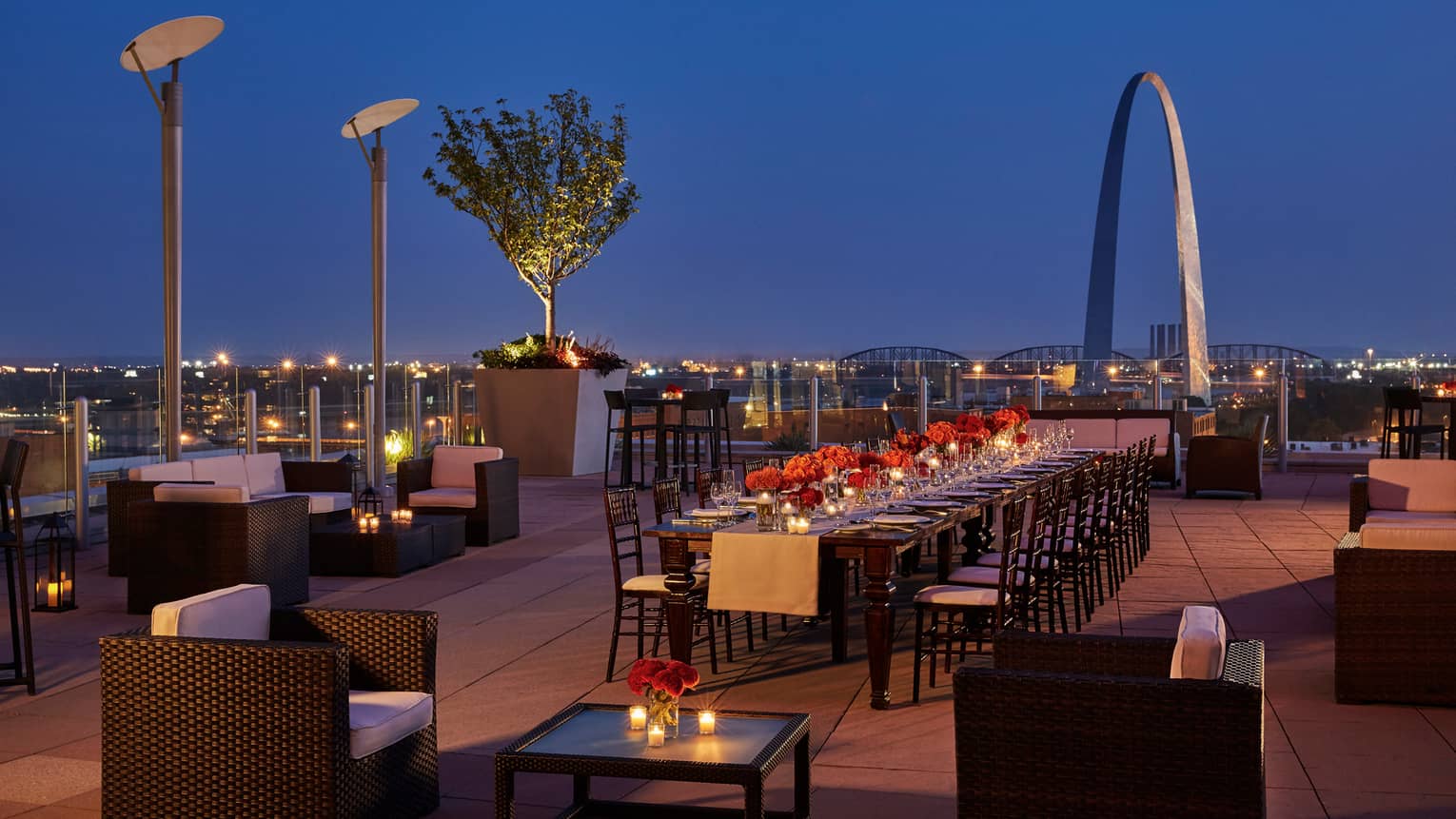 Rooftop patio night view with long, elegant communal table set with red roses, wine glasses and candles