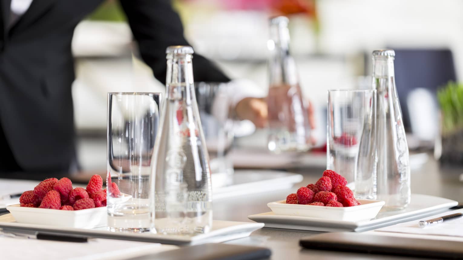 Glass bottles of water and plates of raspberries are set in preparation for a meeting