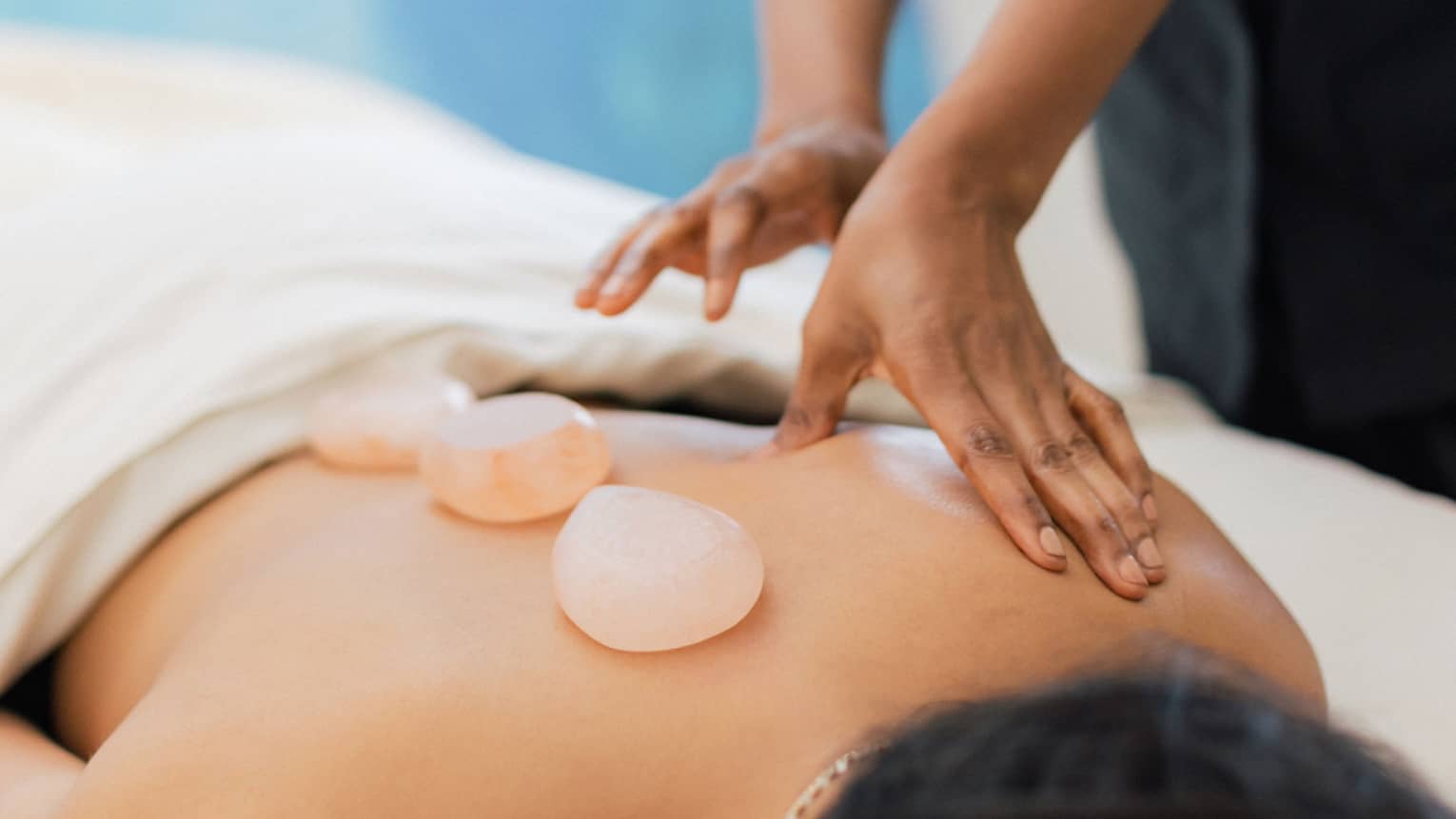 Masseuse places salt stones on a person's bare back