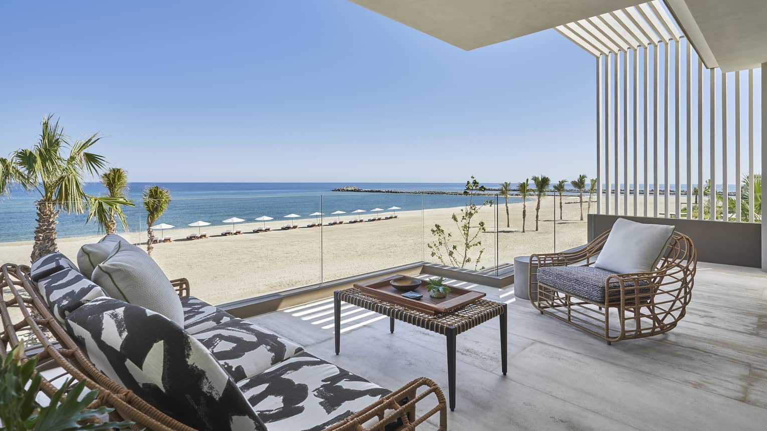 Outdoor terrace with modern wicker sofa and arm chair, glass railing, beach and ocean view