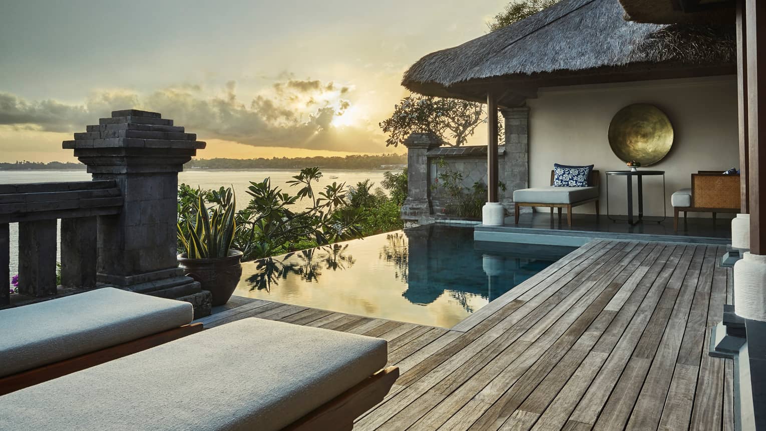 Ocean sunset reflecting on private villa swimming pool, palm trees, thatched roof, lounge chairs