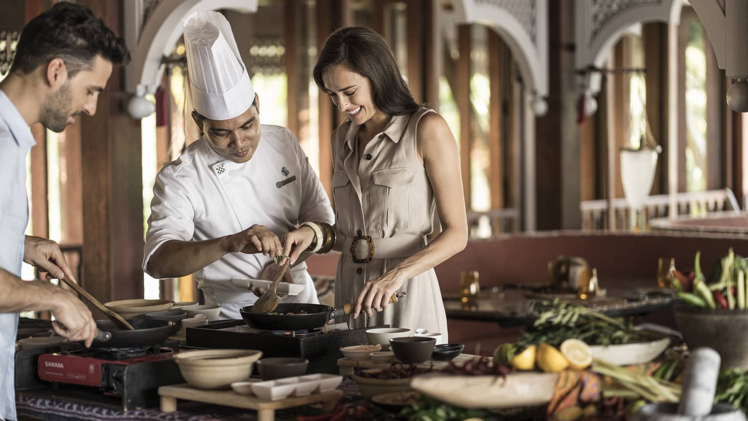 A chef doing an interactive cooking lesson with a man and a woman at the Four Seasons Langkawi