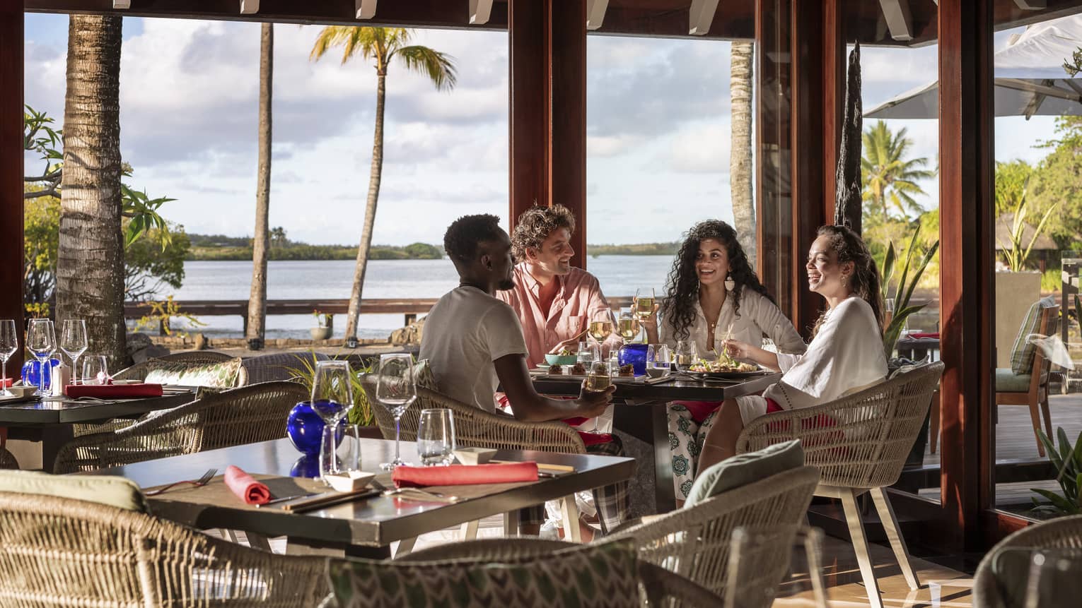 Four friends sitting and talking over food and wine at waterfront restaurant with tall windows