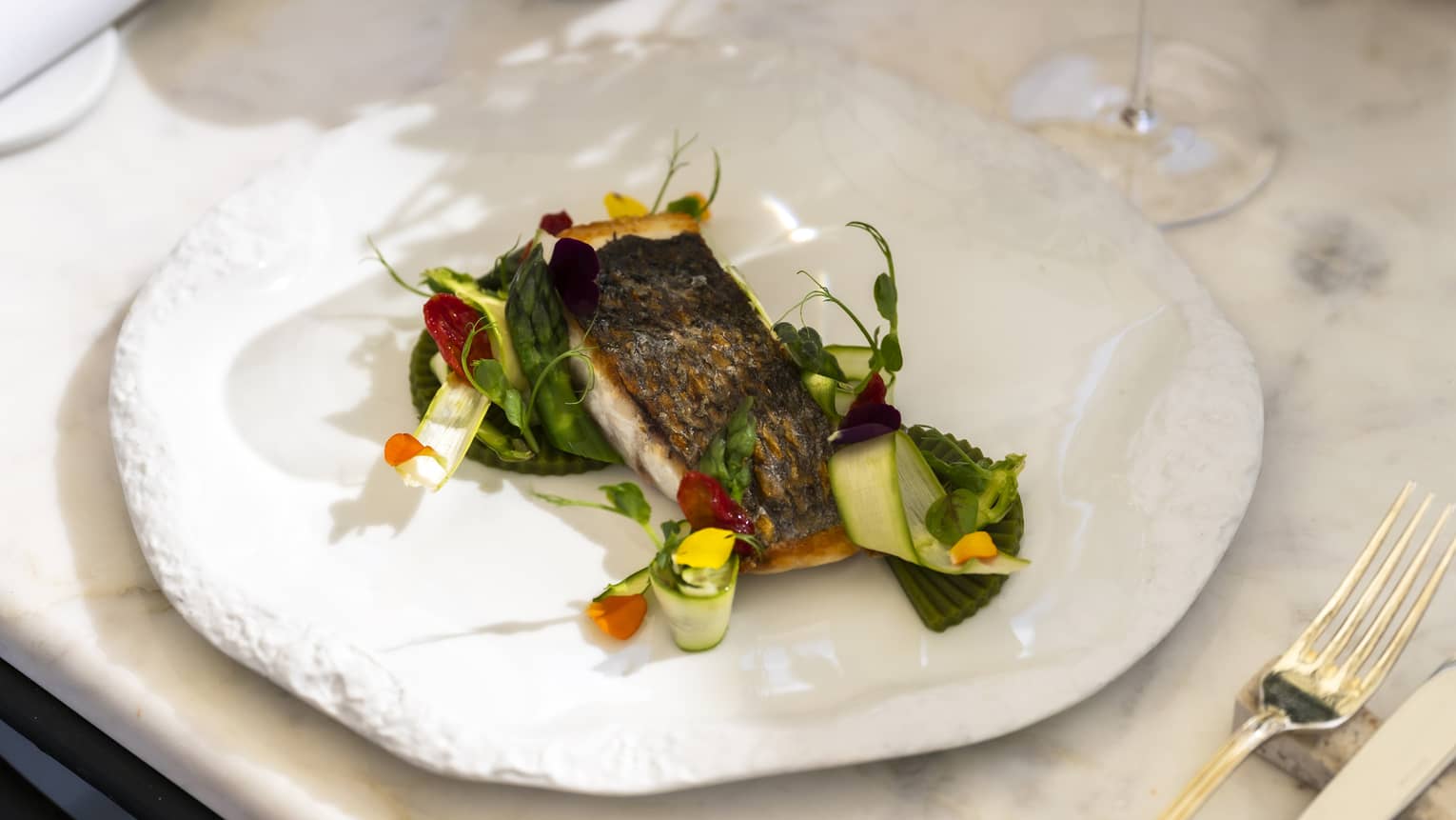 An artistic white plate with a textured rim holds a food item with colourful garnishes.