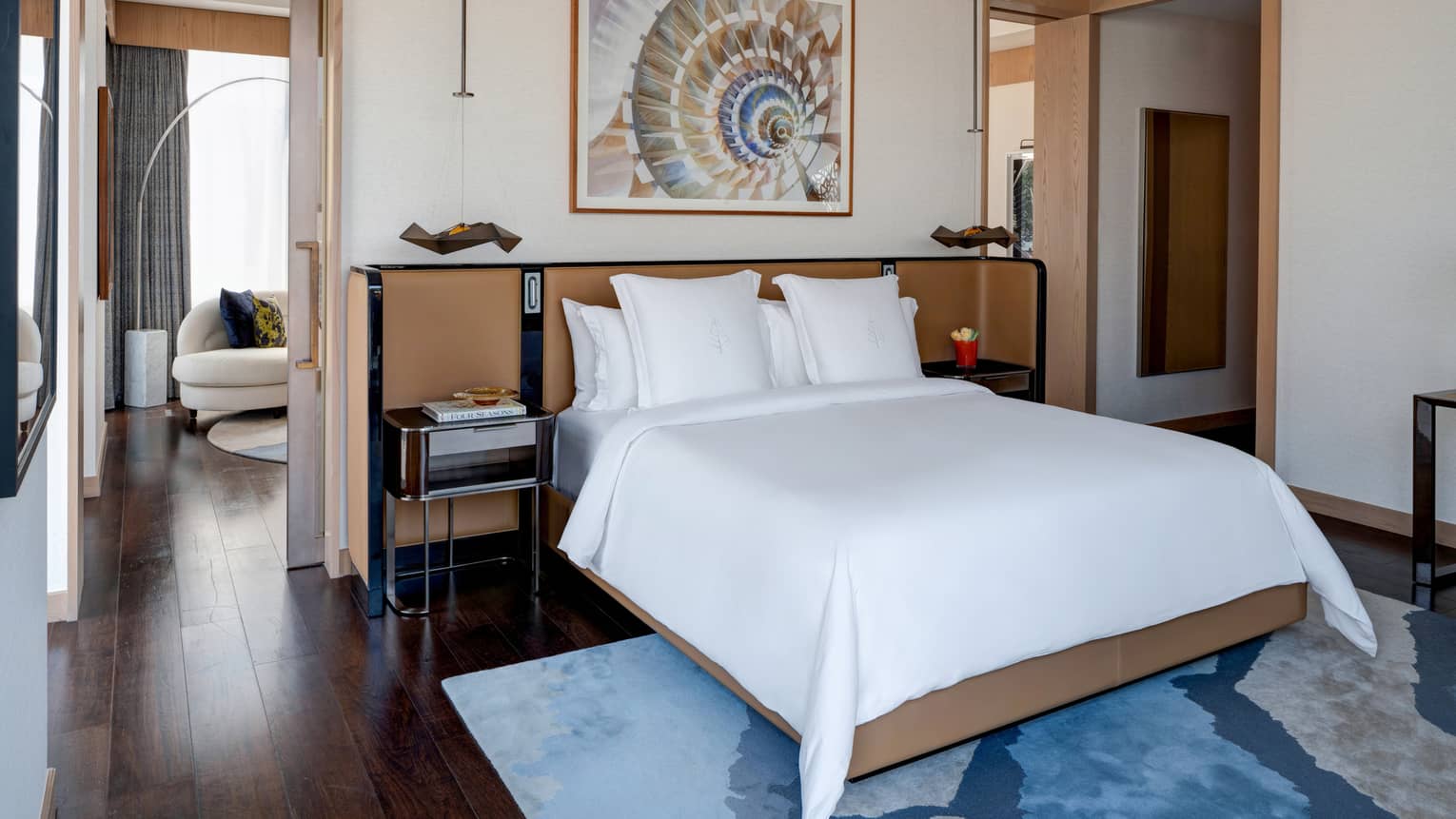 Bedroom with king bed, blue area rug, wooden floors, artwork