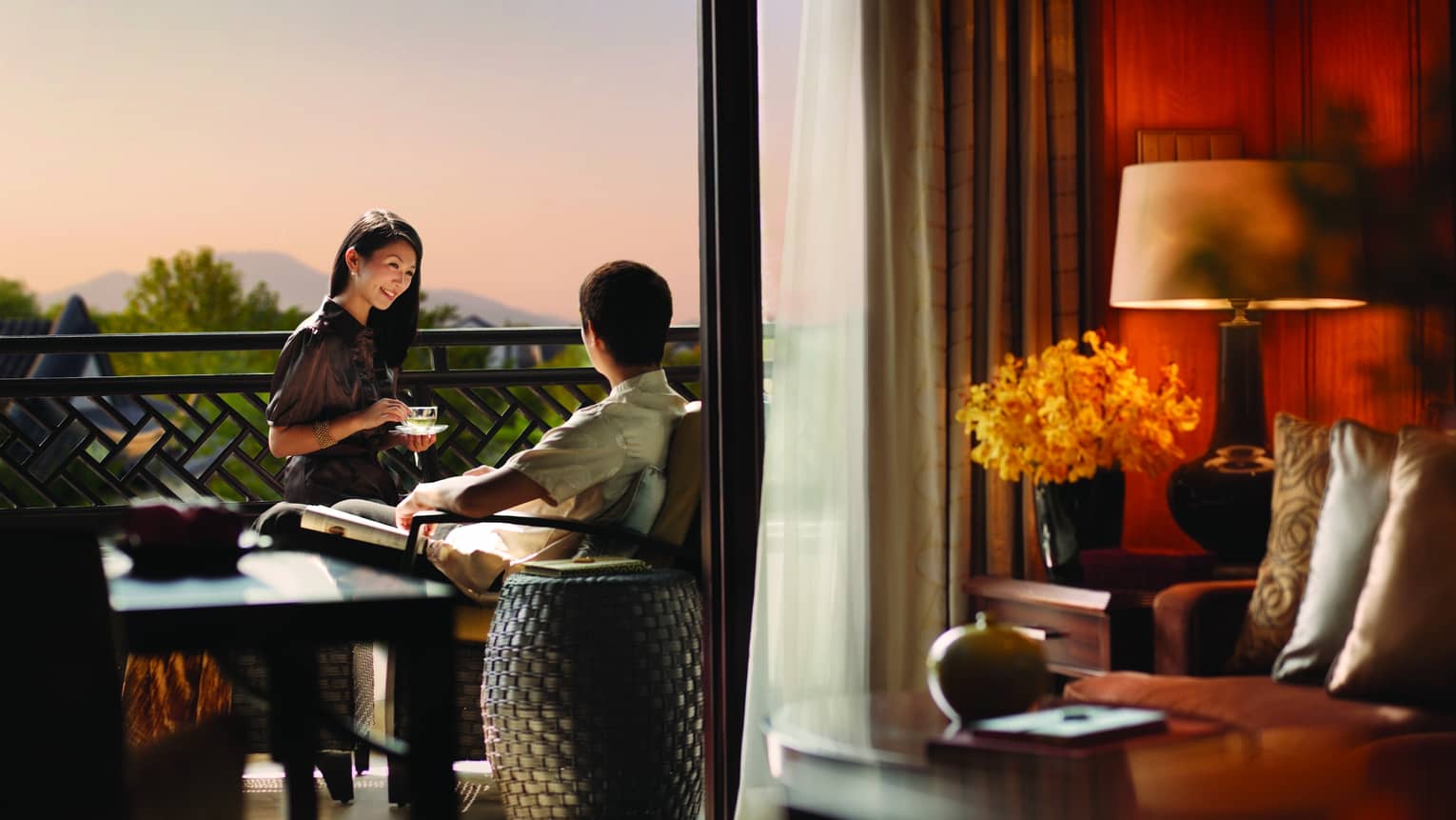 Smiling woman with teacup faces man sitting on hotel room patio