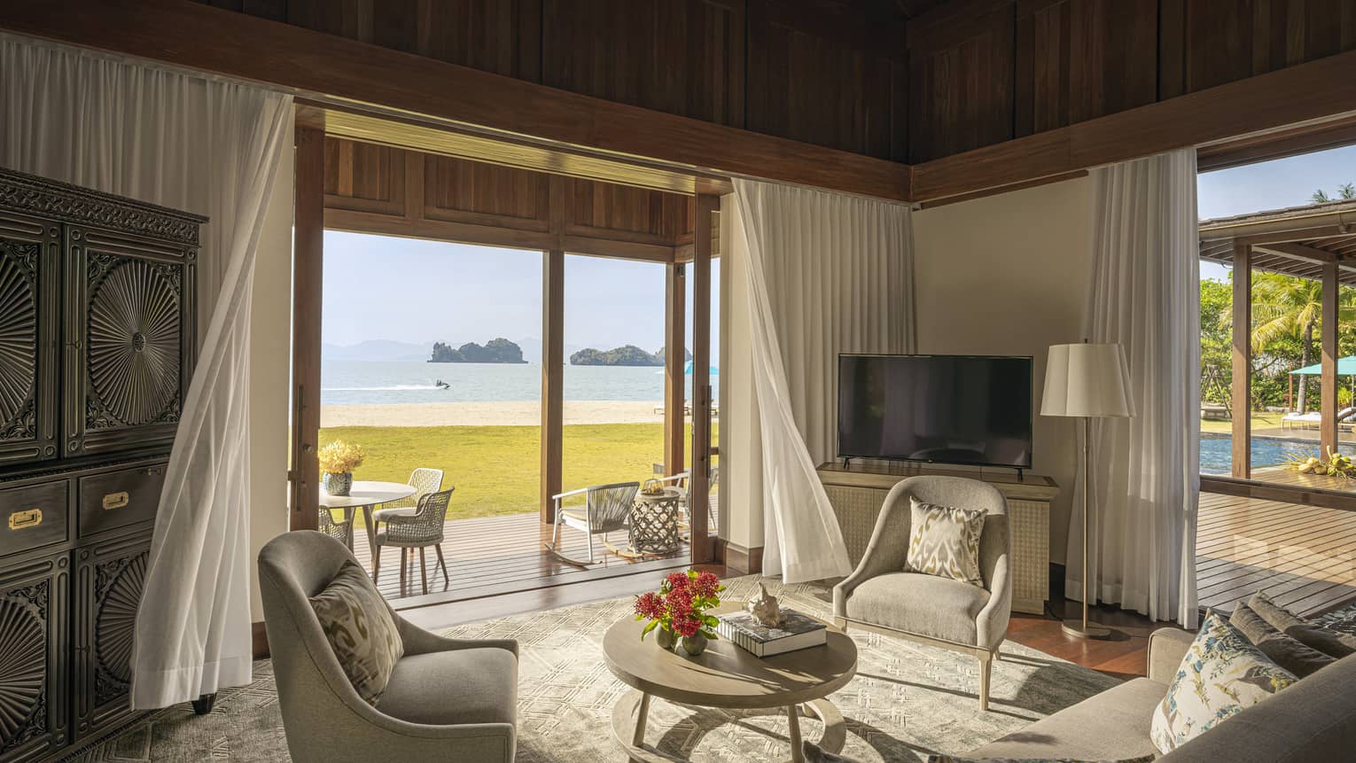 Sitting room with sofa and two chairs, with walk-out wooden terrace and beach view