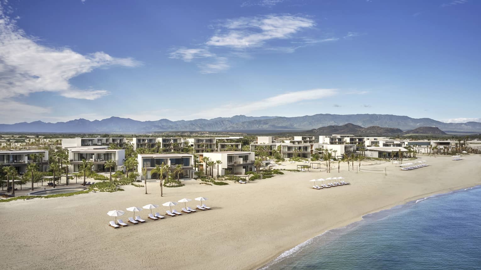 A beach with building and lounge chairs.