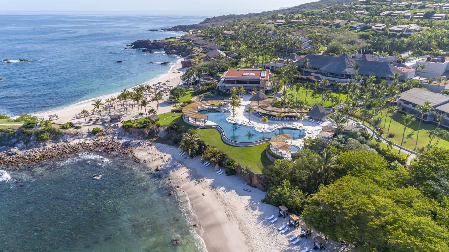 An aerial view of a beach shore with a large property on it with an outdoor pool.