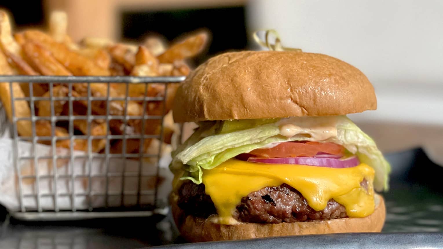 A burger with lettuce, tomato and cheese next to a small basket of fries.