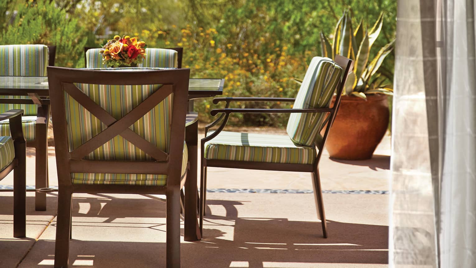 Close-up of iron patio dining table with green striped cushions, fresh flower centrepiece