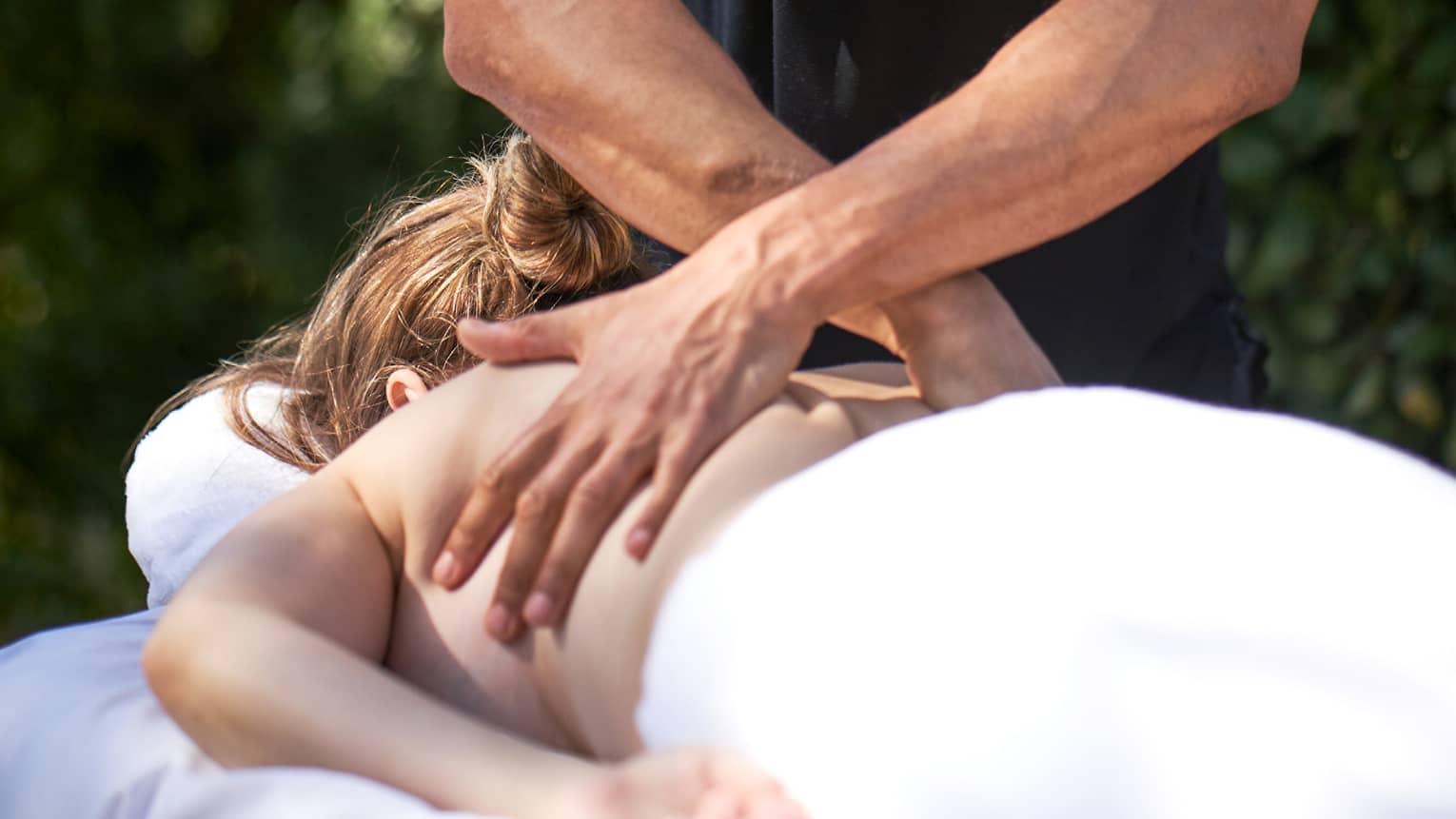 Man crosses hands over woman's back as she lays on outdoor massage table
