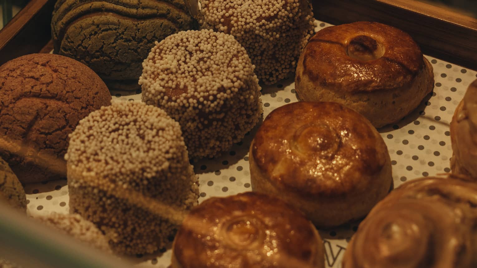 Hand holding silver tongs reaches into a pastry case to grab a small, round cake
