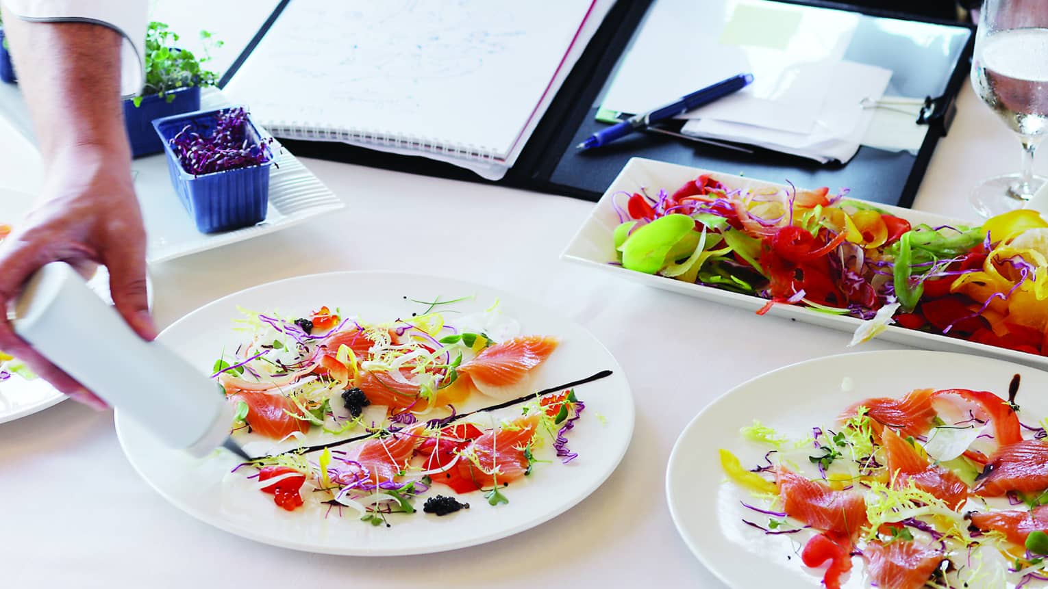 Chef garnishes gourmet entrees at table with open binder 
